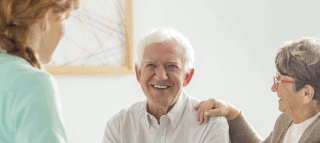 An elderly man and woman smiling and talking to a woman