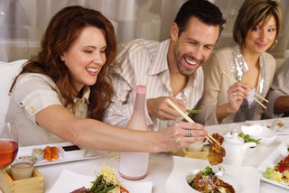 Three people eating with chopsticks, two of whom are laughing