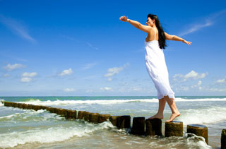 A woman balances on a set of concrete pier posts that extend into the ocean