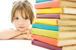 A young girl rests her chin on crossed arms beside a stack of text books
