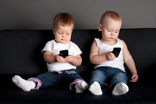 Two babies on a couch playing with mobile phones