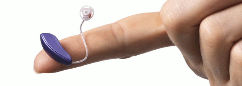 A receiver-in-the-ear style hearing aid on an outstretched finger